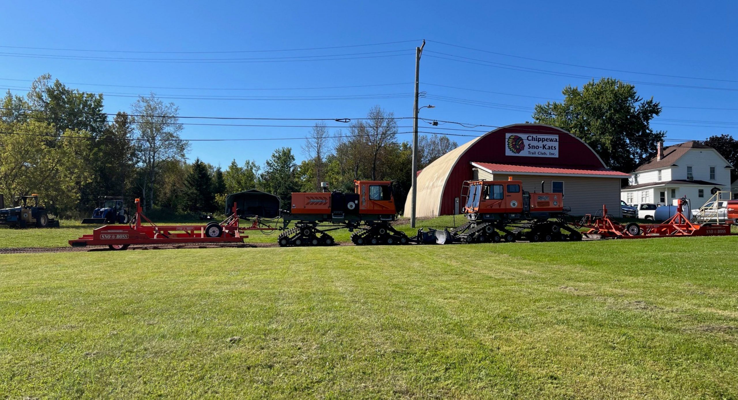 Groomer machines parked in lawn in front of Chippewa Sno-Kats trail club building in summer